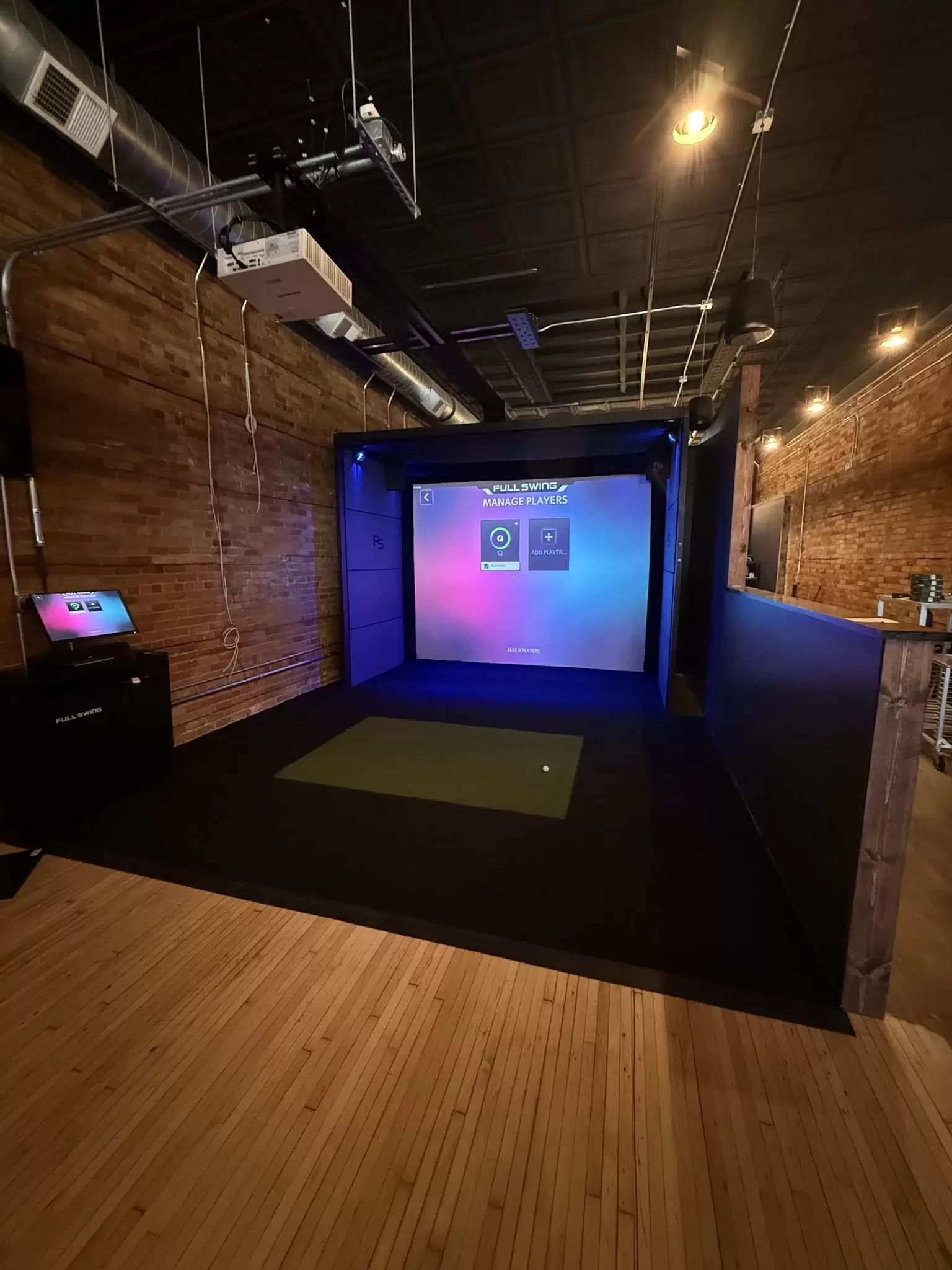 Golf simulator bay with a player kiosk beside the brick wall at Tower Avenue Country Club